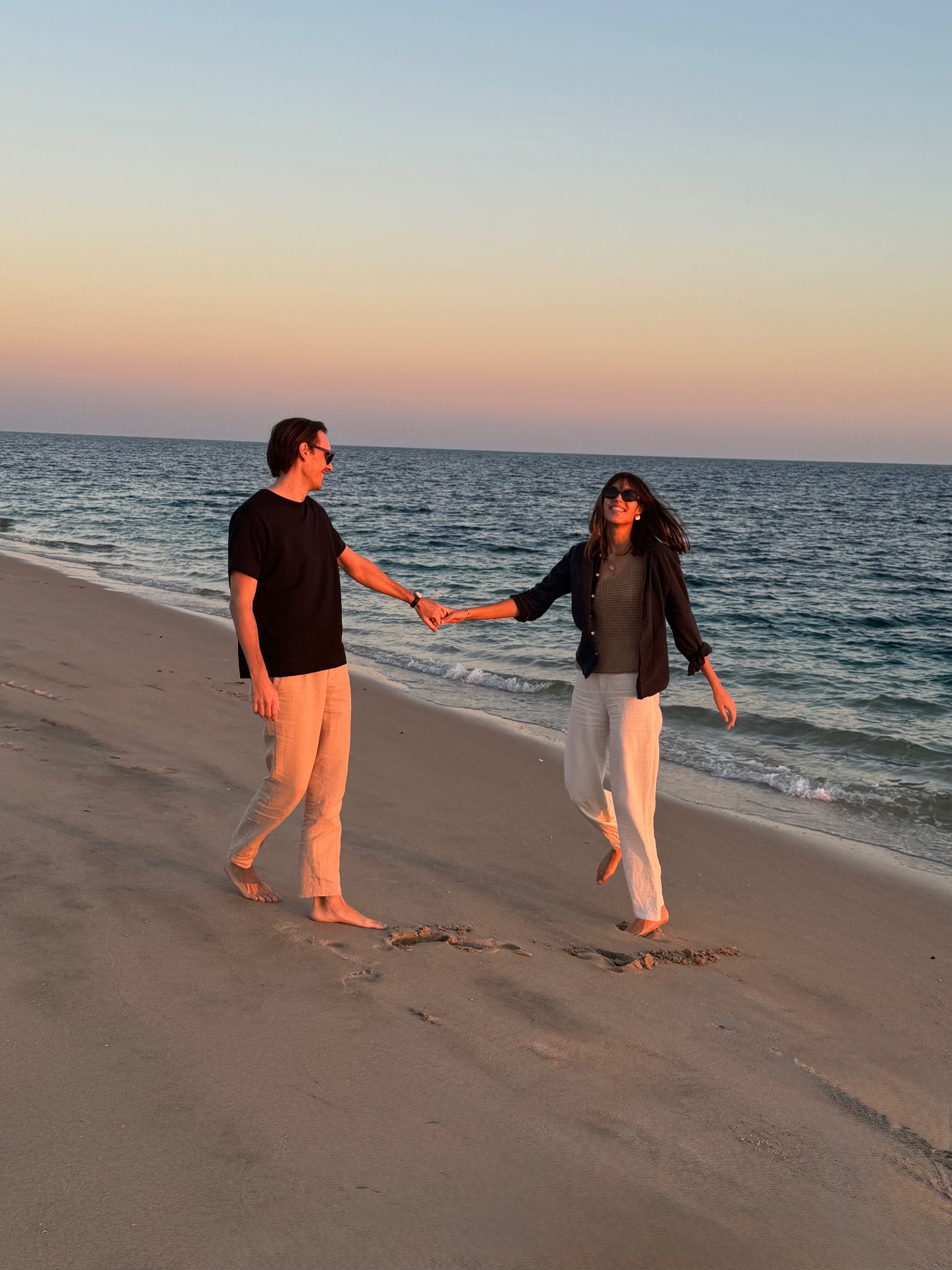 Sabeena and Fabian, founders of August List, walking on a beach at sunset